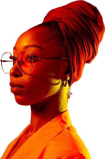 A portrait of a Black woman in side profile, lit with dramatic red and orange lighting against a black background. They wear large round glasses, small hoop earrings, and a tall headwrap that matches their brightly colored clothing. The warm lighting highlights their face and clothing, creating a bold, high-contrast look.